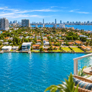 Photo composite of North Bay Village waterfront and Biscayne Bay, with a furnished balcony in the foreground.