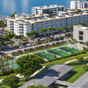Elevated view of green sports courts beside a modern community center in North Bay Village, with residential buildings and waterfront in the background.