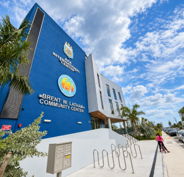 Angled exterior view of the Brent W. Latham Community Center and AFA International Center in North Bay Village, with palm trees and bicycle racks.