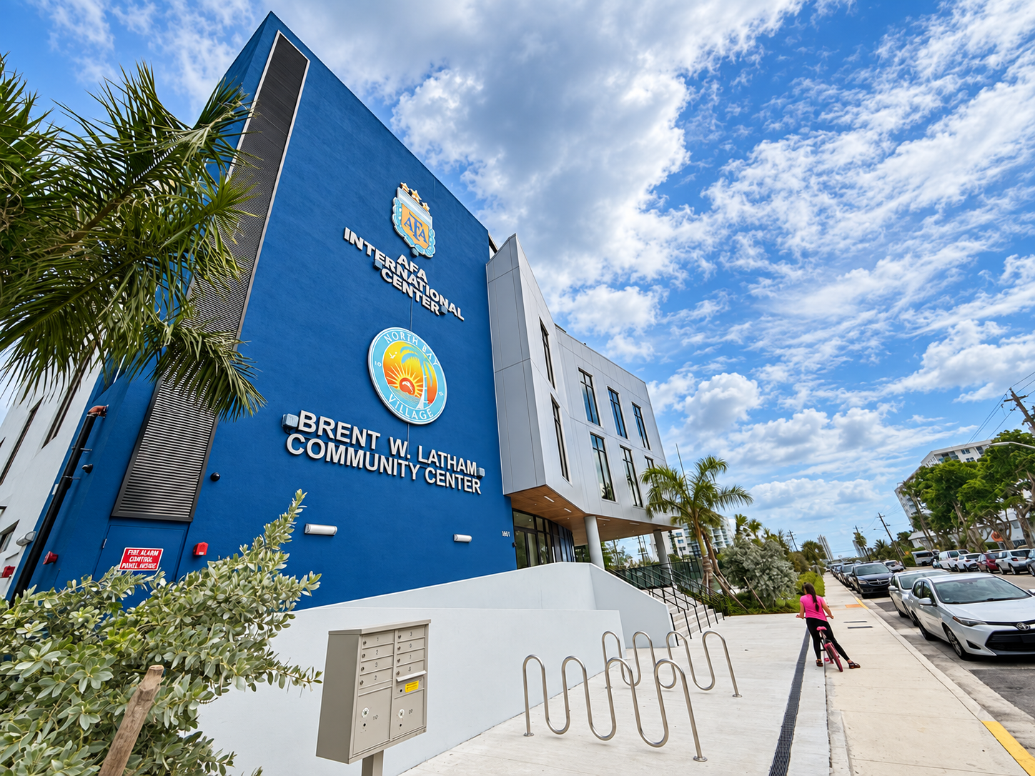 Angled exterior view of the Brent W. Latham Community Center and AFA International Center in North Bay Village, with palm trees and bicycle racks.