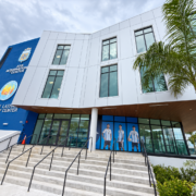 Stairs and railings leading to the glass entrance of the Brent W. Latham Community Center, with Argentina soccer player graphics and palm trees.