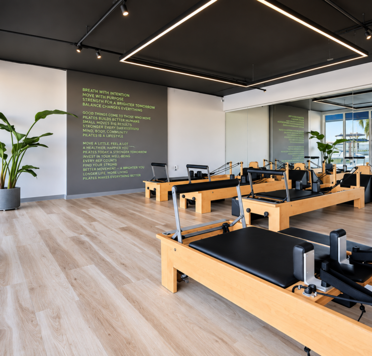 Modern Pilates studio with wooden reformer machines, mirrored walls, natural light, and waterfront views.