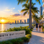 North Bay Village waterfront promenade at sunset with palm trees, Biscayne Bay views, residents walking, and modern waterfront buildings.